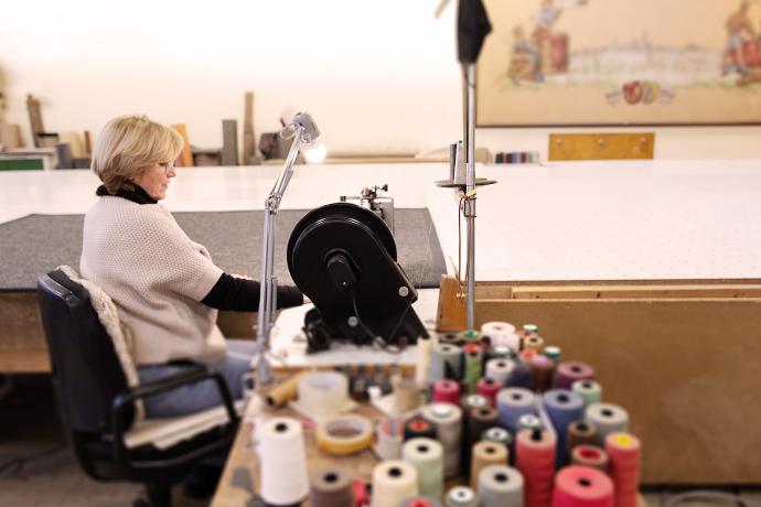 Photo of a woman at a sewing machine edging a sisal rug.